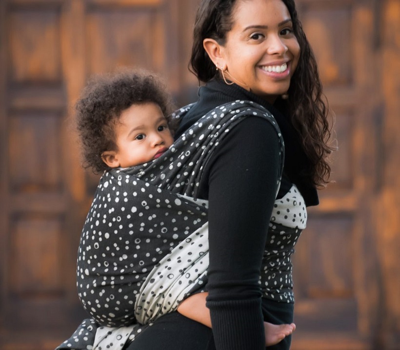 picture of woman walking with a baby on her back wraped in a babywearing 