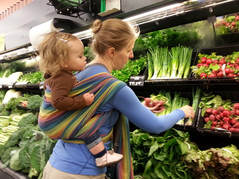 picture of a woman shoping vegetables with a baby on her back in a babywear