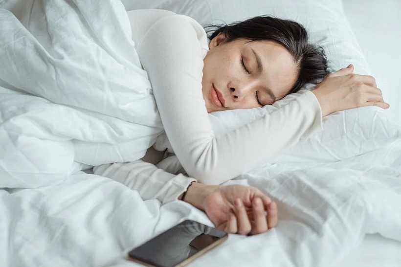 picture of a woman sleeping on a white sheets beside smart phone 