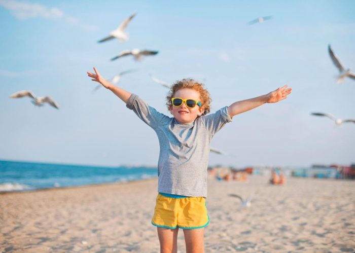 kid spreading his arms wide at the beach with seagulls flying around him