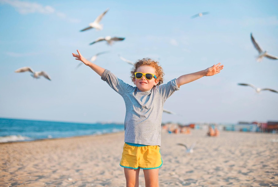 kid spreading his arms wide at the beach with seagulls flying around him